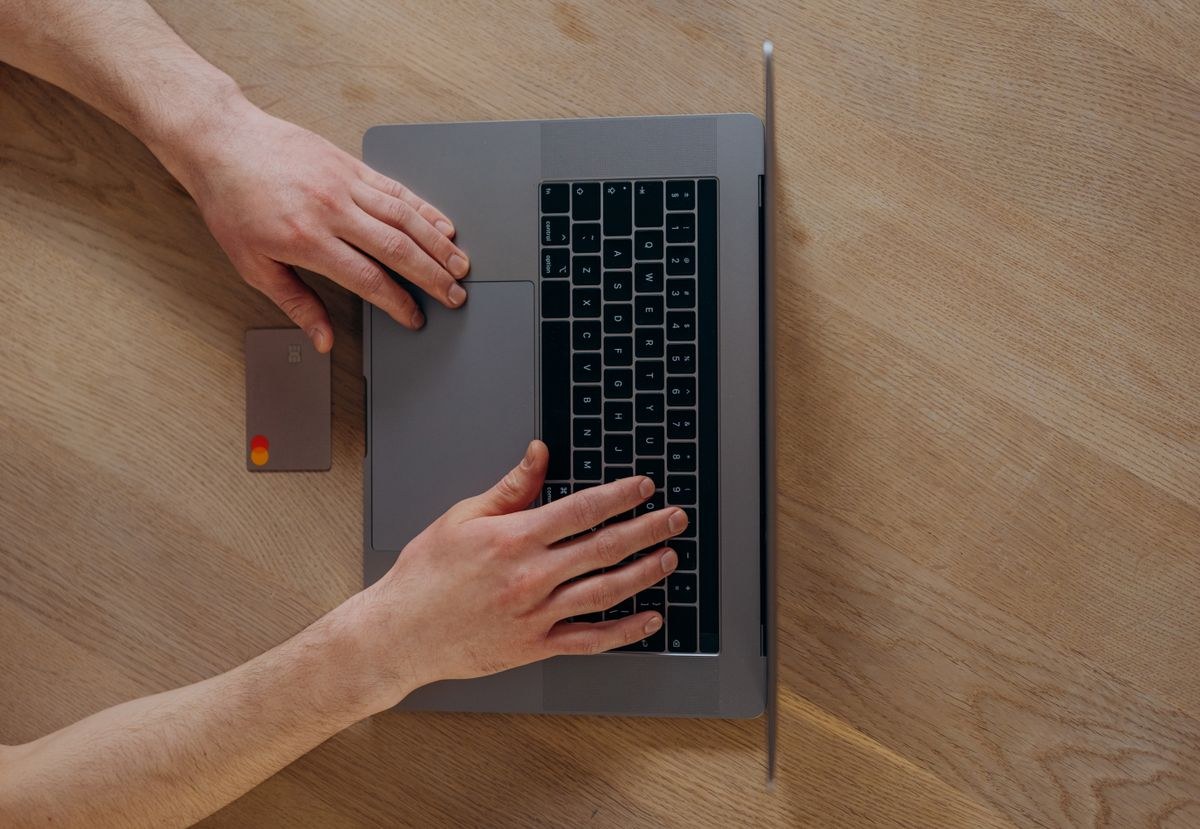 Person using a laptop beside a credit card on a wooden table
